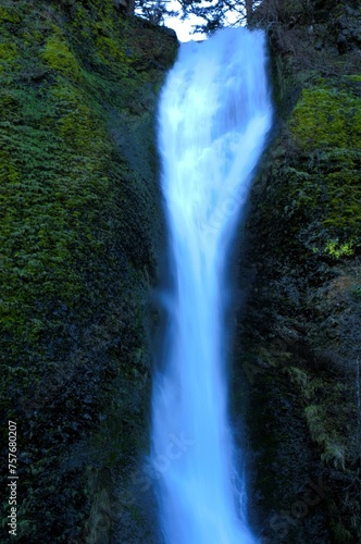 Side view of waterfall streaming between moss covered volcanic rock face.