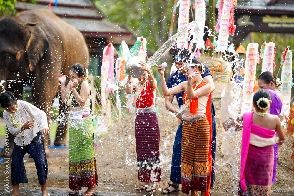 Fototapeta premium Group of Thai women and children ware Thai traditional dress play to splashing water on the Thai New Year's Day or Songkran festival in a fun way on elephant and pile of sand background.