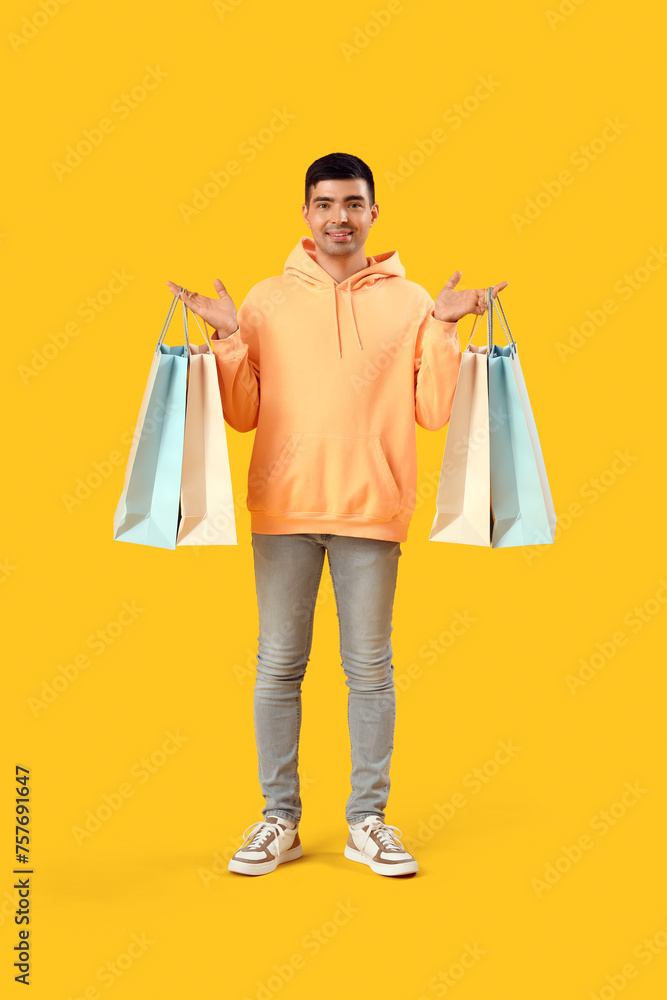 Handsome young man with shopping bags on yellow background Handsome young man with shopping bags on yellow background