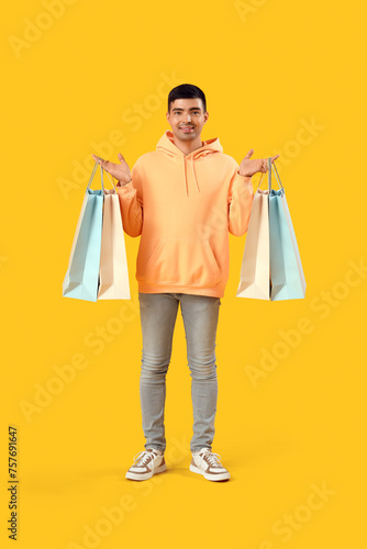 Handsome young man with shopping bags on yellow background