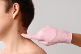 Dermatologist examining moles on young man's neck against light background, closeup