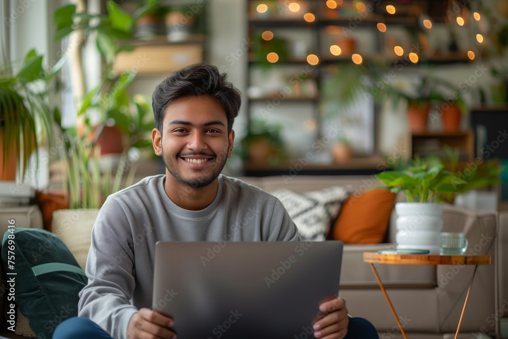 Smiling young man with laptop sitting comfortably at home surrounded by plants and warm lights, concept of remote work and cozy living Smiling young man with laptop sitting comfortably at home surrounded by plants and warm lights, concept of remote work and cozy living