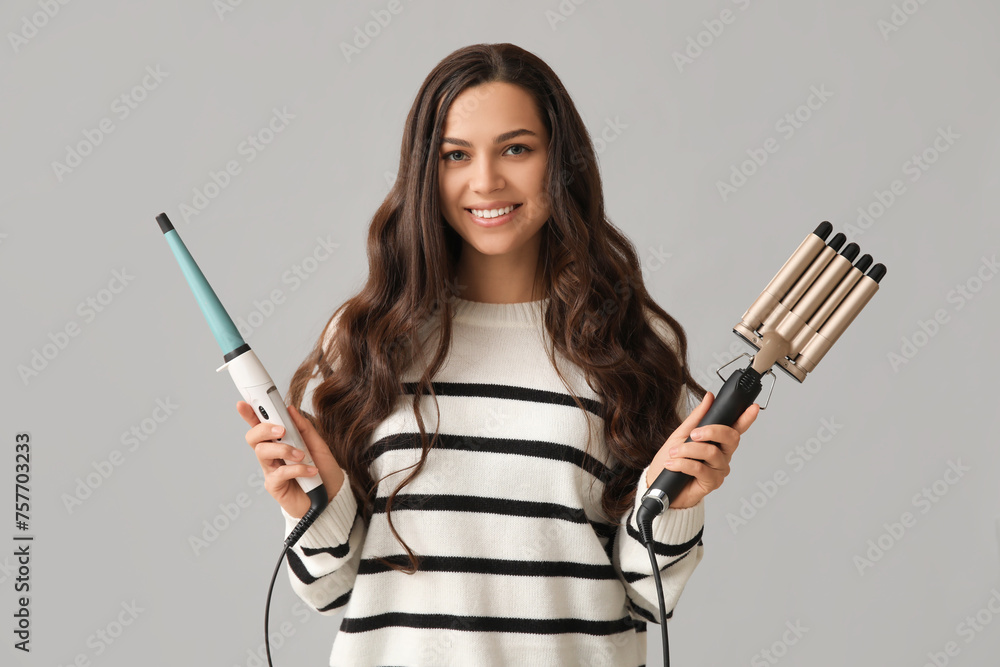 Beautiful young woman with different curling irons on grey background Beautiful young woman with different curling irons on grey background