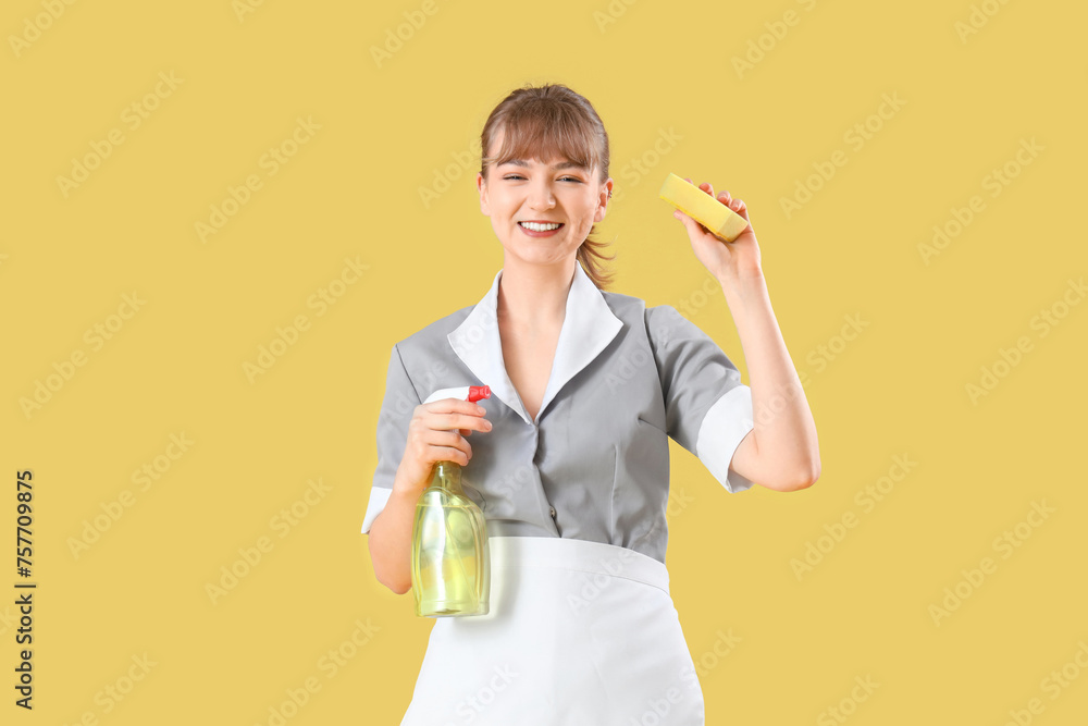 Young chambermaid with cleaning sponge and detergent on yellow background Young chambermaid with cleaning sponge and detergent on yellow background