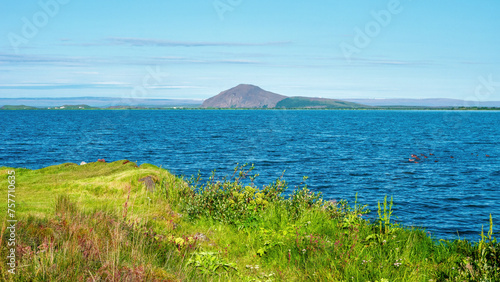Panorama with a volcanic mount at Myvatn lake shore at sunny day and blue sky with copy space