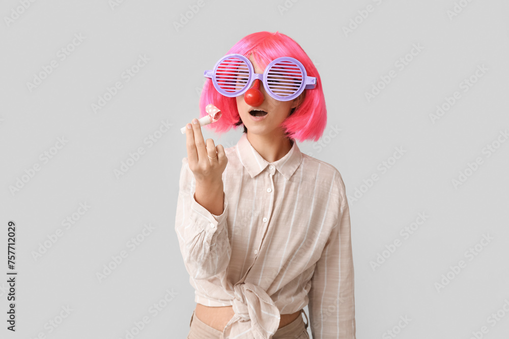 Beautiful young shocked woman in funny disguise with party whistle on grey background. April Fools Day celebration Beautiful young shocked woman in funny disguise with party whistle on grey background. April Fools Day celebration