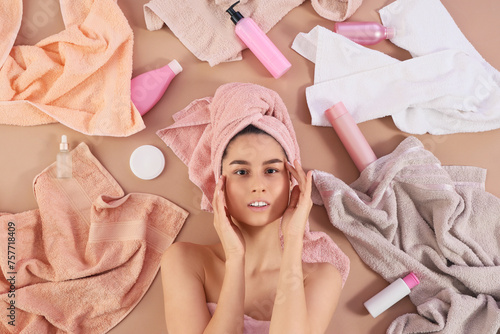 Young woman with towels and cosmetic products after shower on beige background