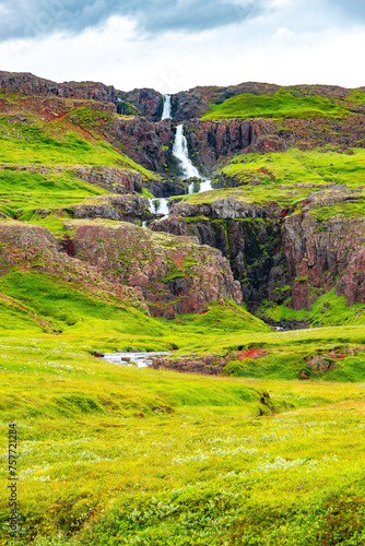 Cover page with cascading waterfall in East Iceland, with dramatic sky and green meadow hills. Beautiful Icelandic landscape, huge cliff, water cascade and rock in moss