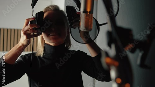Beautiful blonde girl singing song in recording studio with professional microphone and headphones, creates new track album, vocal artist photo