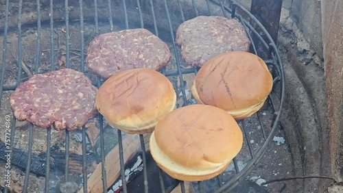 Close up of three buns being roasted next to deer burgers over deep dire pit burning wood for deep rich smoke flavor. photo