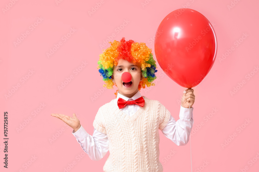 Surprised little boy in clown wig and nose holding balloon on pink background. April Fools Day celebration Surprised little boy in clown wig and nose holding balloon on pink background. April Fools Day celebration