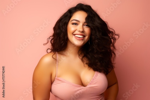 Portraitof a radiant plus-size female model, age 25, Hispanic, smiling brightly against a gentle pink backdrop, showcasing beauty and positivity