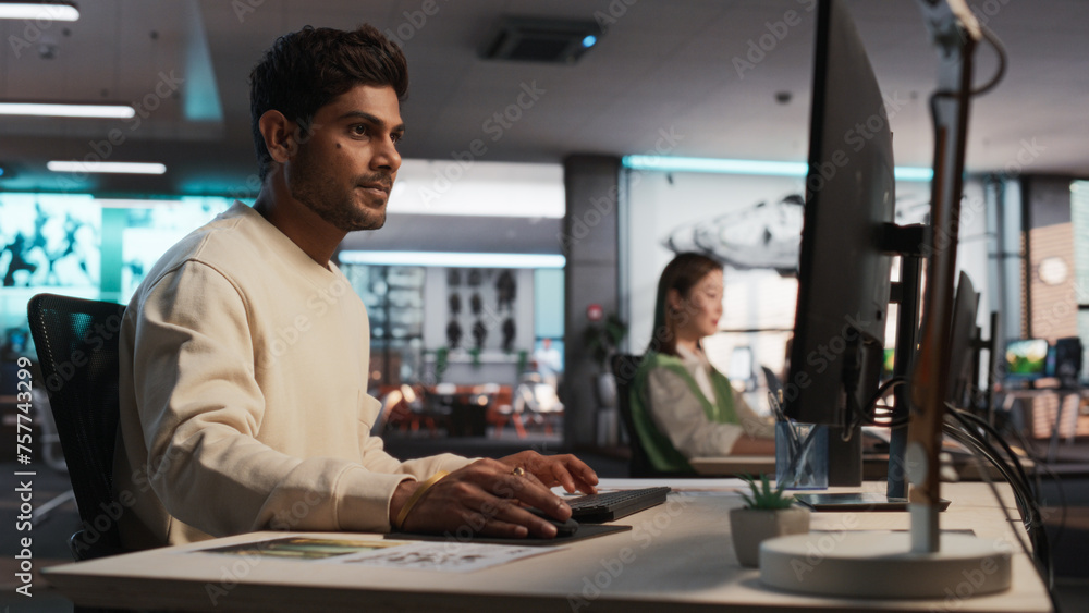 Indian Male Game Designer Using Desktop Computer With 3D Modelling Software To Design Unique Characters And World For Immersive RPG Video Game. Man Working In Game Development Company Diverse Office Indian Male Game Designer Using Desktop Computer With 3D Modelling Software To Design Unique Characters And World For Immersive RPG Video Game. Man Working In Game Development Company Diverse Office