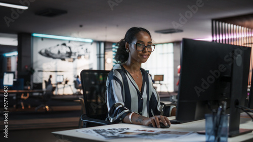 Young Black Woman Working on Desktop Computer in Creative Office. Multiethnic Marketing Manager Writing Email Messages, Developing Social Media Strategy, and Researching Project Plan Details Online photo
