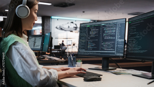 Female Asian Game Programmer Coding On Desktop Computer In Game Development Studio Diverse Office. Focused Woman Writes Lines Of Code. Gameplay Engineer of New Immersive 3D Survival Video Game Working