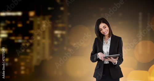Image of businesswoman using digital tablet over glowing spots of light and cityscape