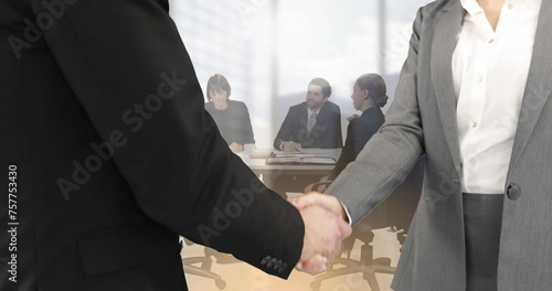 Image of businessman and businesswoman shaking hands over group of businesspeople in office
