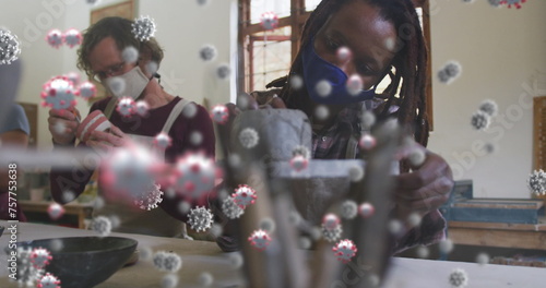 Image of virus cells over diverse workers with face masks painting pottery
