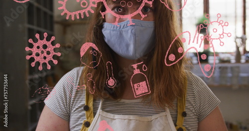 Image of covid icons and cells over woman wearing face mask holding clay in pottery workshop