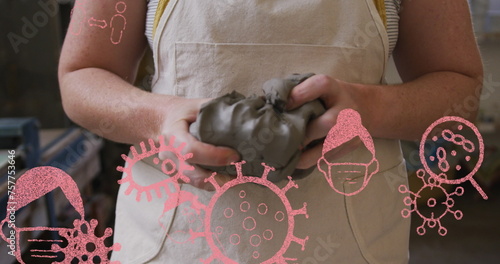 Image of covid icons and cells over woman wearing face mask holding clay in pottery workshop