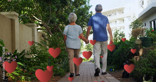Image of falling hearts over caucasian senior couple walking