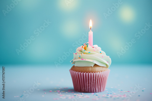 Cupcake with frosting, sugar sprinkles and burning birthday candle in front of blue background