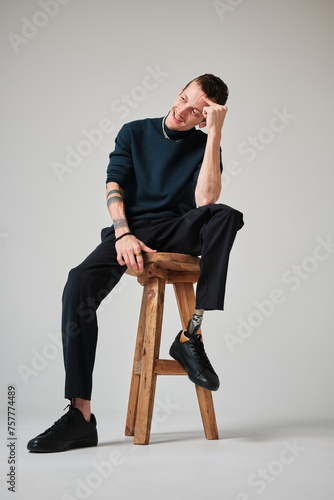 Studio portrait of a successful happy tattooed one legged disabled young male amputee with prosthetic leg wearing casual dark blue clothing. 
