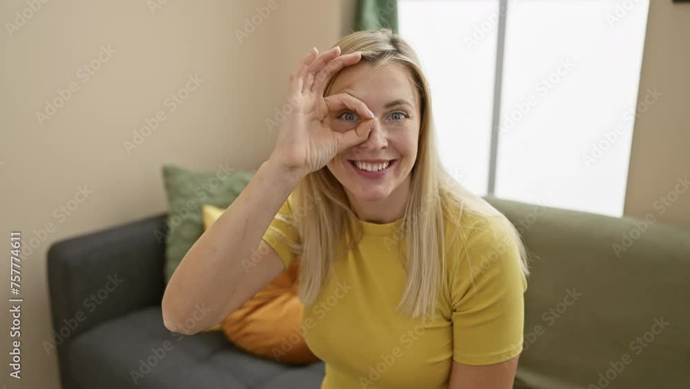 Shocked home look, young, attractive blonde woman does 'ok' gesture through fingers, viewing with surprised face. wearing t-shirt in living room, fun expression of 'wow' shock! Shocked home look, young, attractive blonde woman does 'ok' gesture through fingers, viewing with surprised face. wearing t-shirt in living room, fun expression of 'wow' shock!