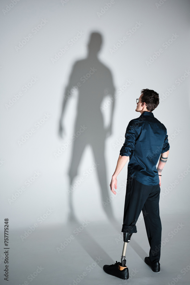 Obraz premium Studio portrait of a successful happy tattooed one legged disabled young male amputee with prosthetic leg wearing casual dark blue clothing. 