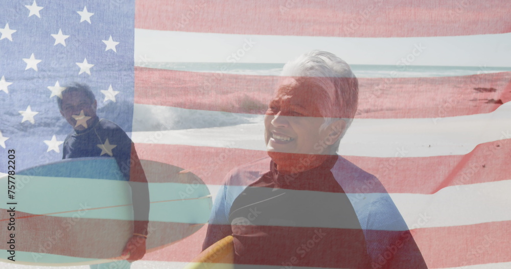 Obraz premium Image of flag of united states of america over senior biracial couple with surfboards on beach