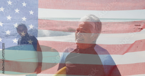 Image of flag of united states of america over senior biracial couple with surfboards on beach