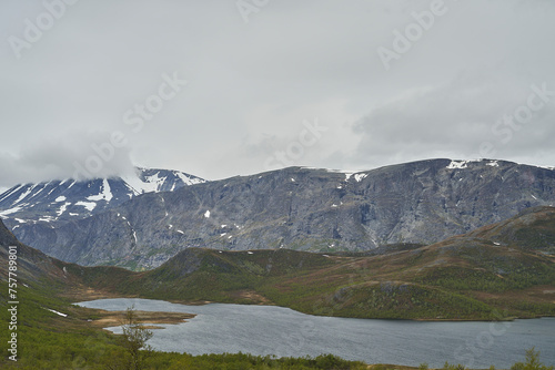 lake in the mountainous landscape of Jotunheimen in Norway, with snow covered peaks in the background, a popular travel destination for hiking.