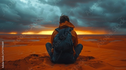 A man sits on a sandy beach with a backpack on his back