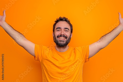 A man in an orange shirt is smiling and raising his arms in the air