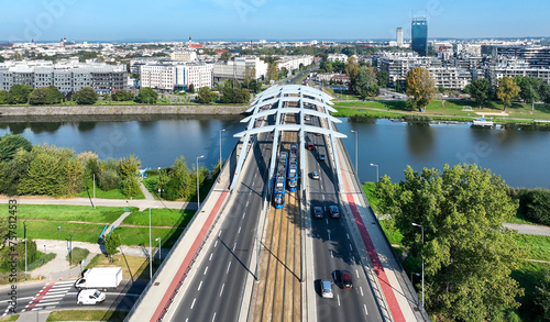 Krakow, Poland. Two blue trams passing each other on Kotlarski suspension bridge with four lane road, tramway, footbridge and red bicycle lane over Vistula river. Aerial view