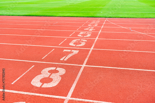 Red running track with green grass in stadium. Athletic competitions starting line positions from one to nine. © Jitti