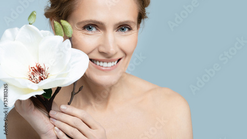 Middle-aged woman showcasing elegance with white magnolia flower on blue backdrop