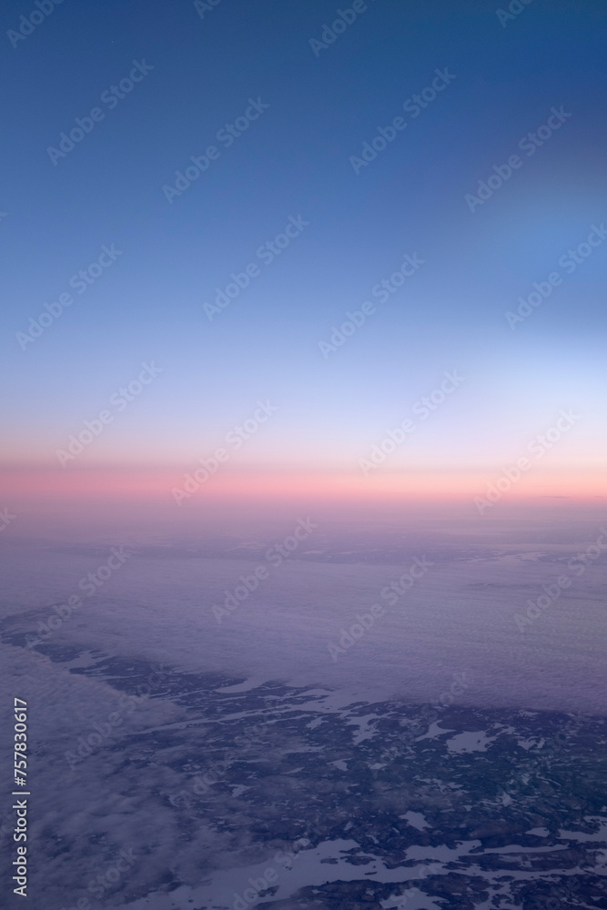 Orange sunset sky on a cloudscape seen from an airplane window over a snowy landscape 