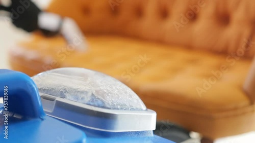 Slow motion of a specialized wet vacuum cleaner as it cleans a sofa. Focus on the water tank within the vacuum cleaner for efficient cleaning.