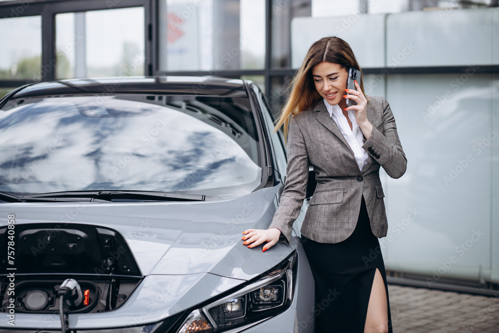 Business woman charging electric car and using mobile phone Business woman charging electric car and using mobile phone