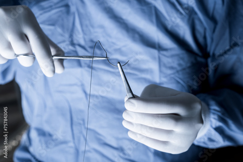 An operator holding half circle with needle holder during operation. Medical professional in scrubs handling sutures. 