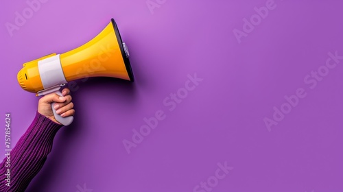 A hand in a purple sweater holding a yellow megaphone against a purple background photo