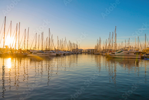 Beautiful port of Alicante at sunrise, Spain at Mediterranean sea. Luxury yachts, ships, ferries and fishing boats sailing and standing in rows in harbor. Rich people traveling around the world.