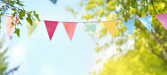Colorful pennant string decoration in green tree foliage on blue sky, summer party background