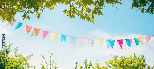 Colorful pennant string decoration in green tree foliage on blue sky, summer party background