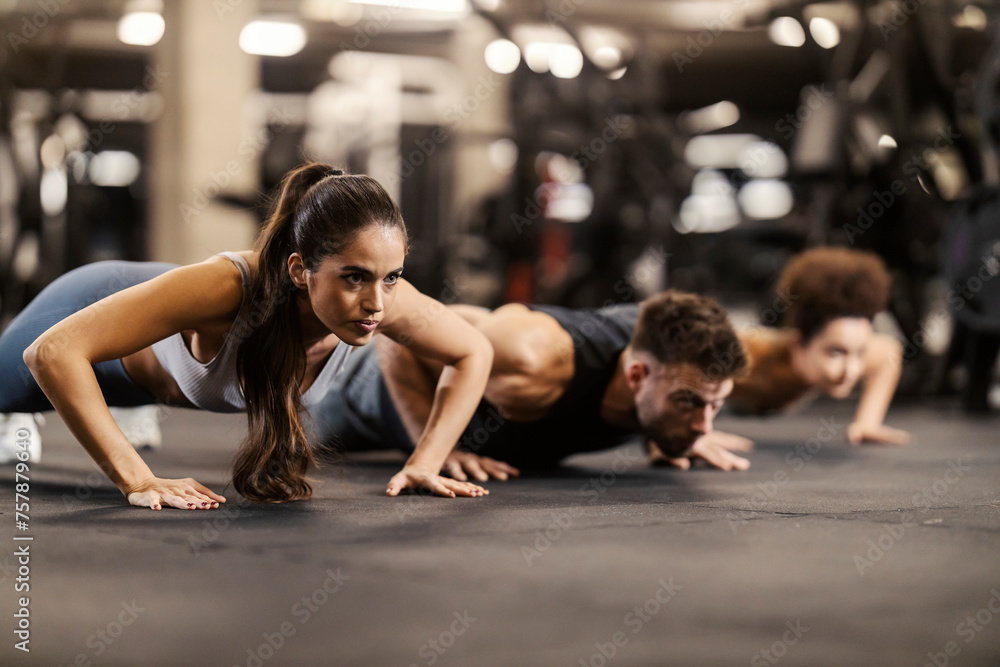 Sportspeople doing pushups in a gym. Selective focus on a sportswoman. Sportspeople doing pushups in a gym. Selective focus on a sportswoman.