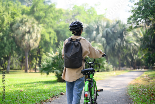 Rear view of young woman walking with bicycle in a sunny park. Lifestyle, transportation, and ECO friendly concept photo