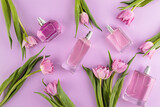 A set of perfume bottles of various shapes on a lilac background with delicate pink tulips. Flat lay. Top view. Presentation of spring fragrances