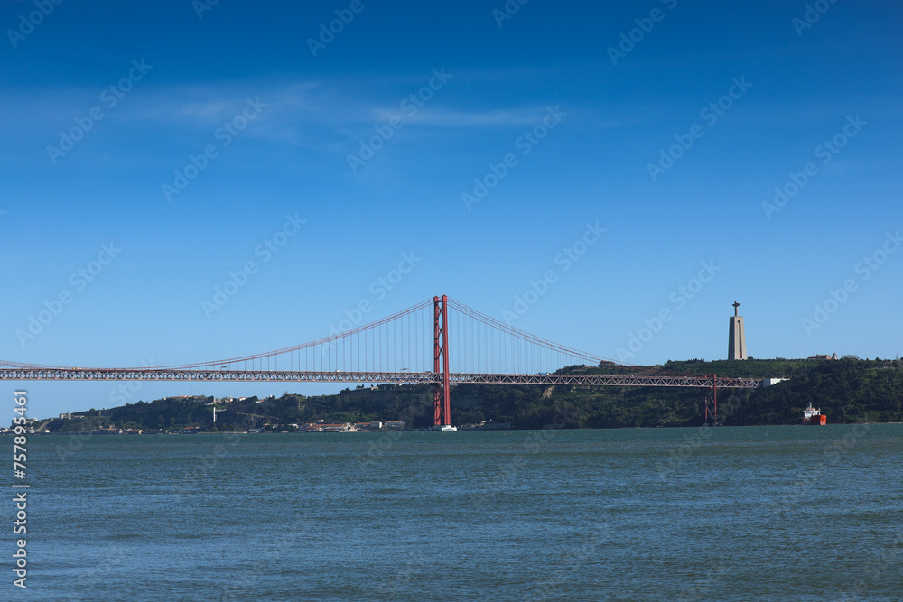 25 April Bridge and the statue of Jesus over Tagus River. Landmarks from Lisbon, Portugal, during a sunny day with blue sky.