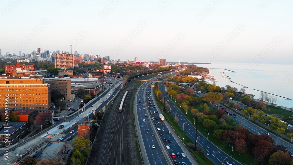 Top view of approaching train and highway traffic jam at sunset. Wide view of skyscrapers, green trees, calming lake and cars that are stuck in traffic jam. Leave early to avoid traffic jam on road.